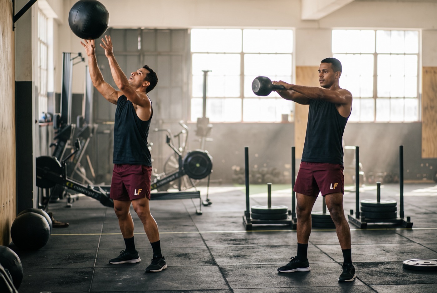 Dois alunos num treino funcional, com bola e kettlebell